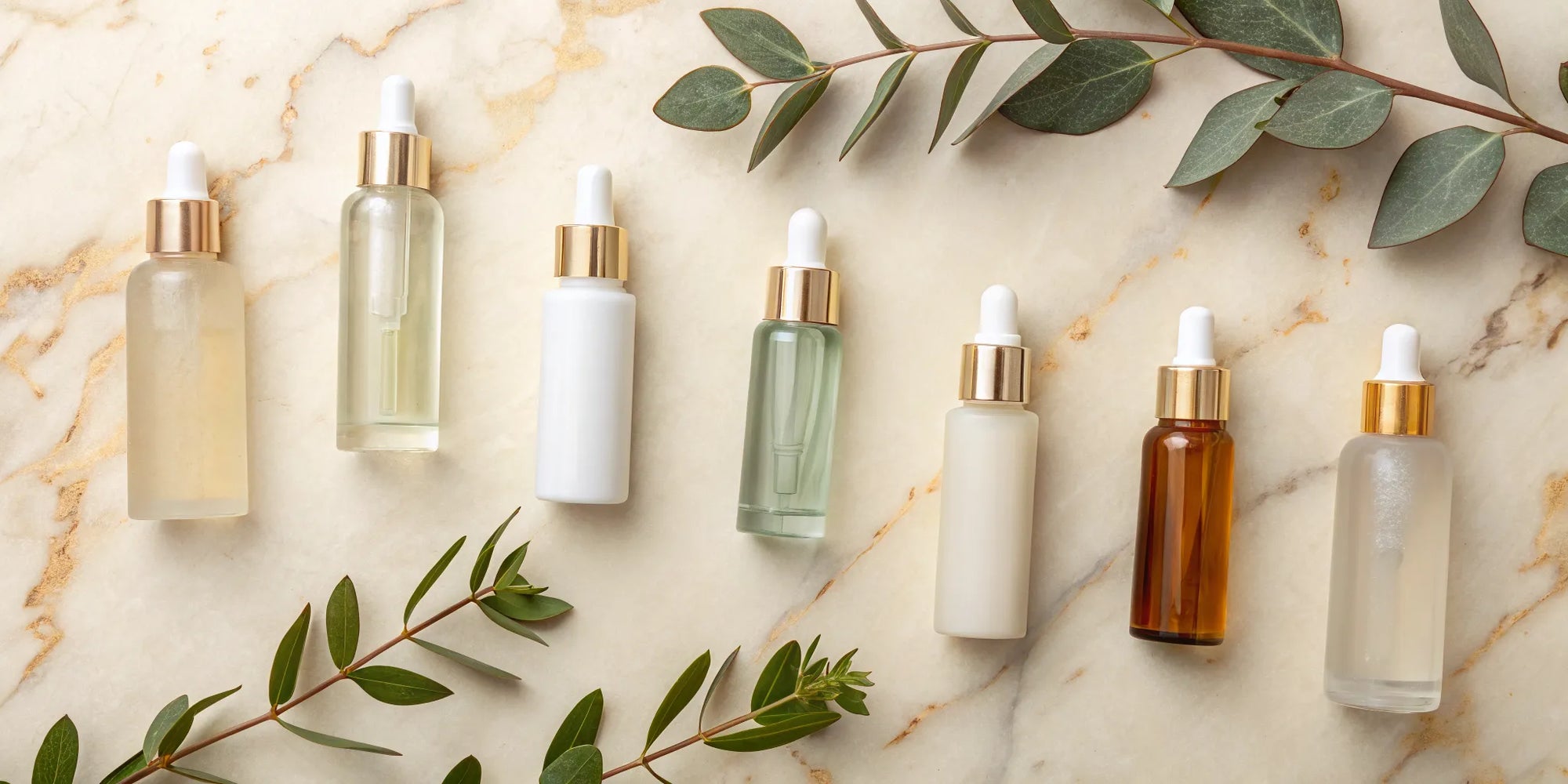 Plant-based luxury skincare serums with gold droppers and green leaves on a marble background.